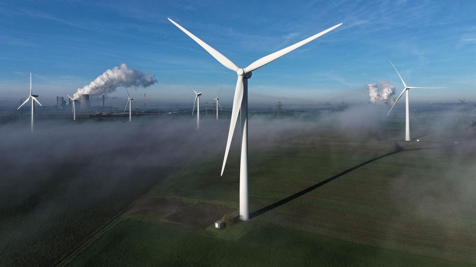 Auf dem Bild sind mehrere Windräder in Bergheim zu sehen, im Hintergrund auch zwei Kohlekraftwerke.