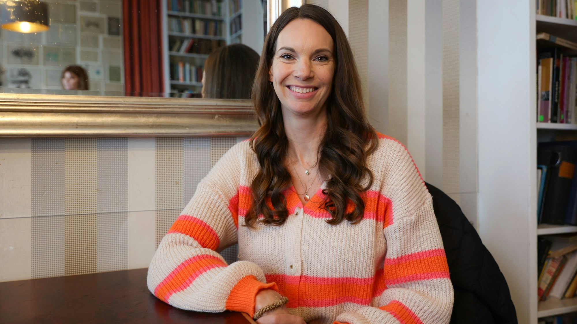 Eine Frau sitzt lächelnd an einem Tisch in einem Café.