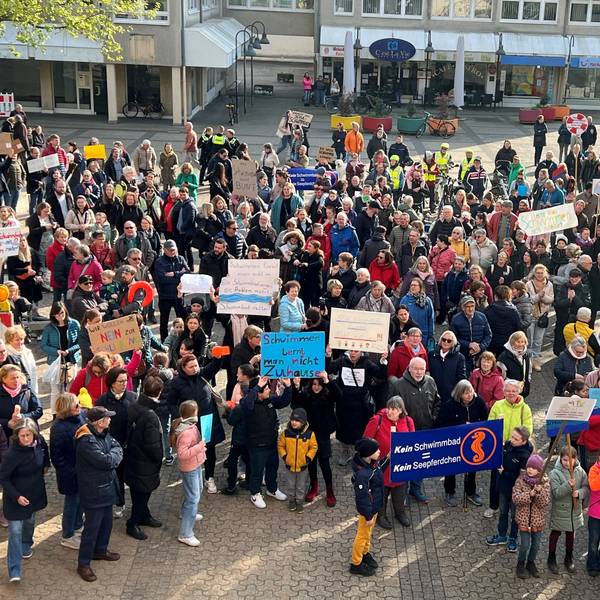 Auf dem Foto sind protestierende Menschen zu sehen. Sie halten Plakate gegen die Schließung des Schulschwimmbads hoch.