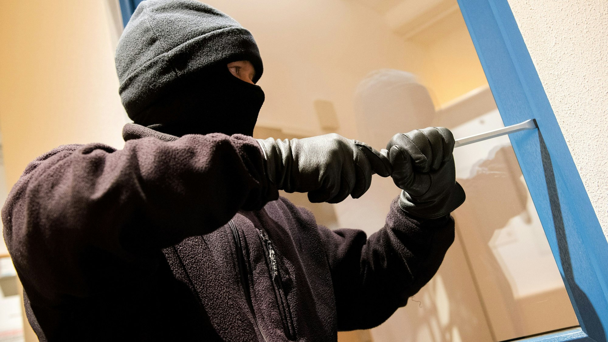 Ein als Einbrecher verkleideter Mann hebelt in einer Kriminalpolizeilichen Beratungsstelle der Polizei ein Fenster auf.