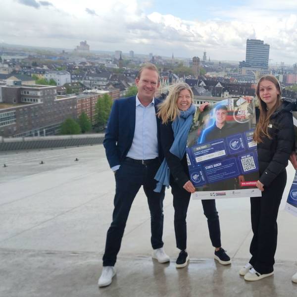 Zwei Männer und zwei Frauen stehen mit Plakat auf einem Dach, im Hintergrund ist der Dom zu erkennen
