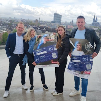 Zwei Männer und zwei Frauen stehen mit Plakat auf einem Dach, im Hintergrund ist der Dom zu erkennen