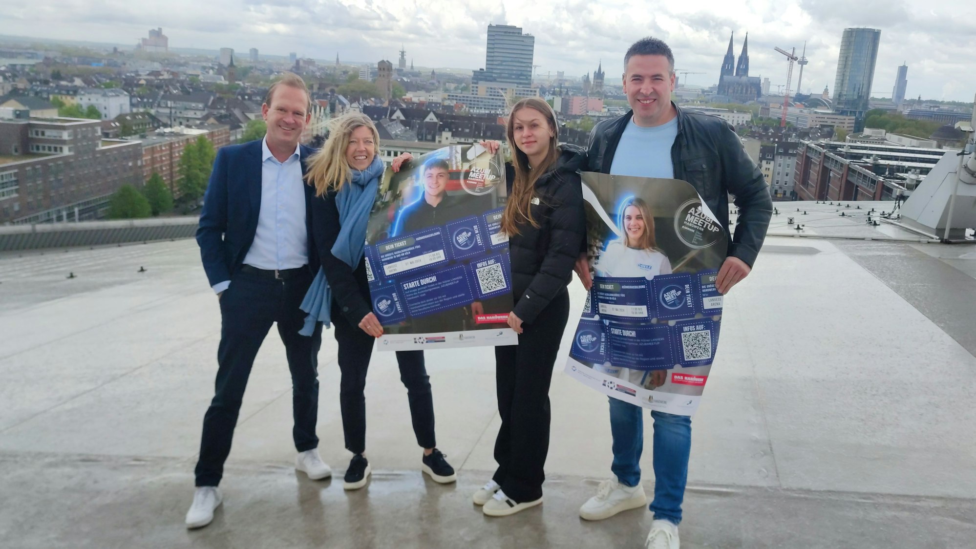 Zwei Männer und zwei Frauen stehen mit Plakat auf einem Dach, im Hintergrund ist der Dom zu erkennen