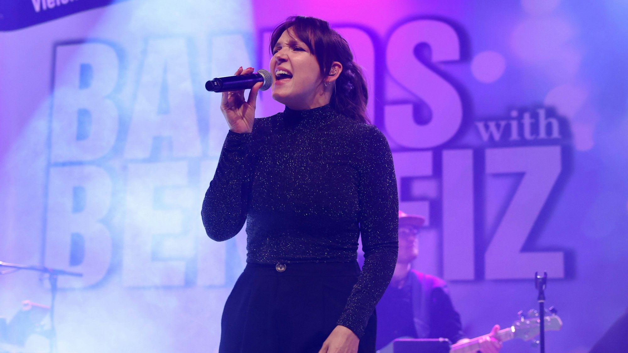 Carolin Kebekus steht auf einer Bühne und singt in ein Mikro.