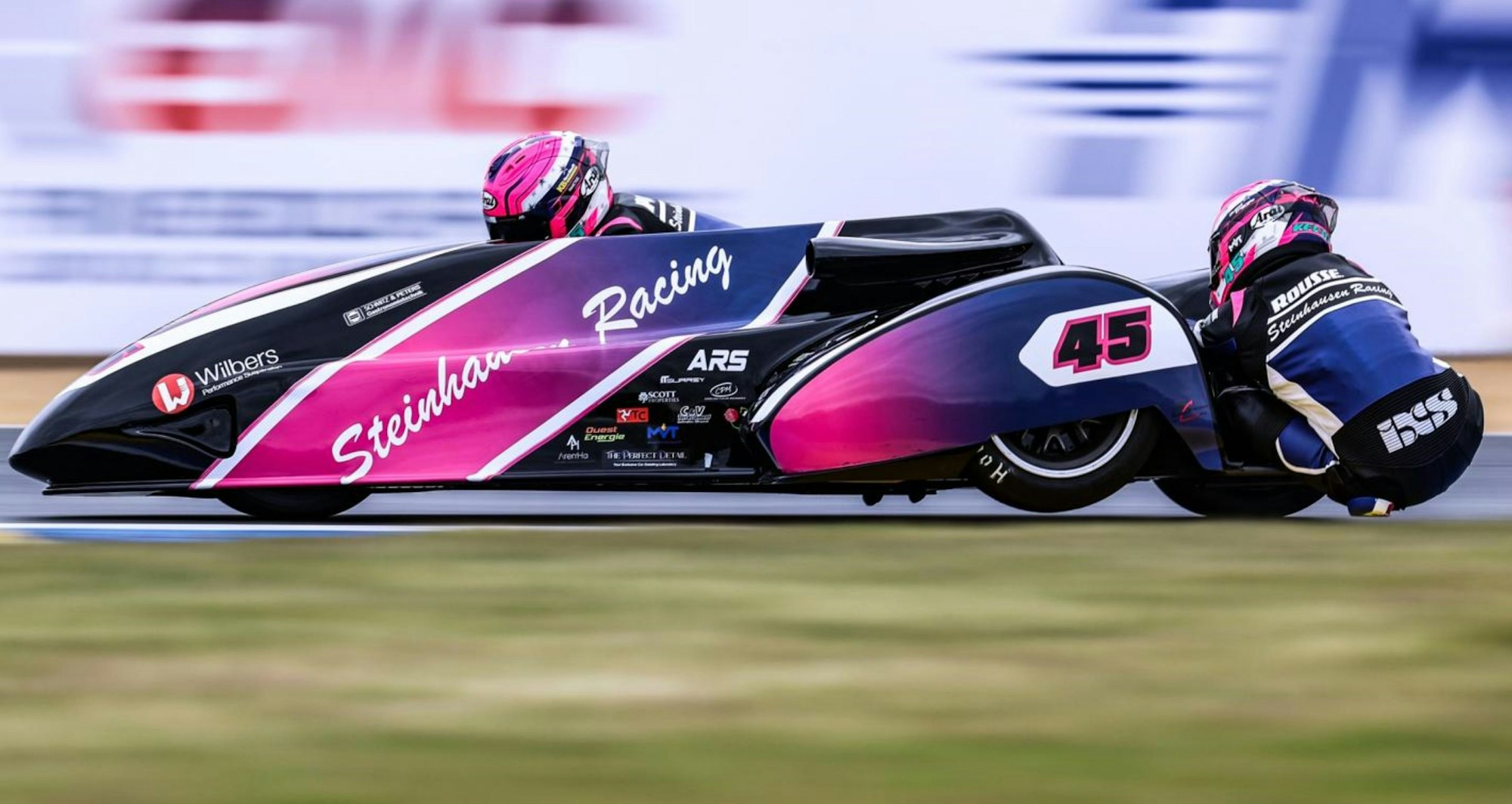 Eine Rennszene mit Fahrer Harry Payne und Beifahrer Kevin Rousseau, der sich aus dem Seitenwagen hängt.