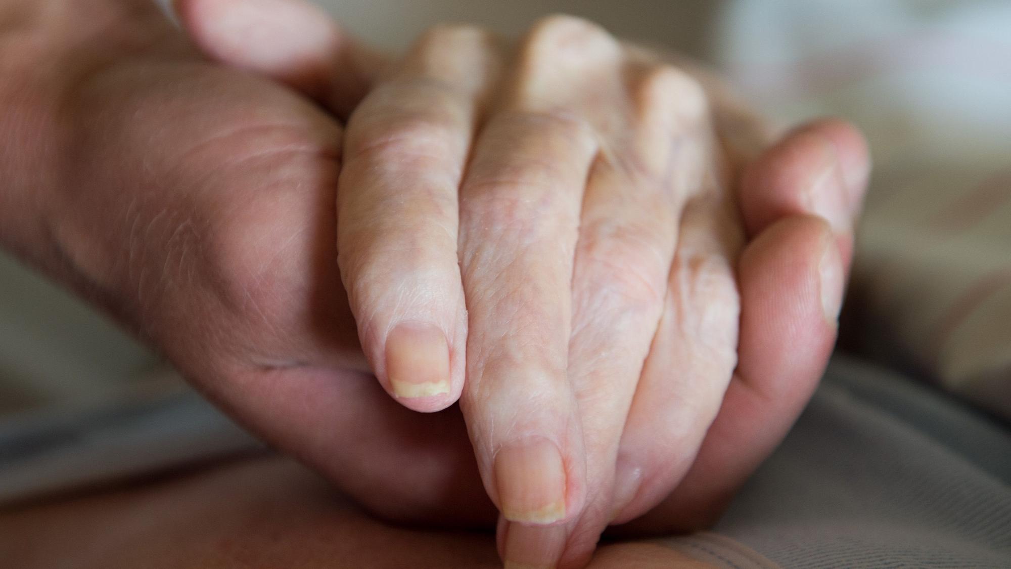 Ein Altenpfleger hält in einem Pflegeheim die Hand einer Frau.