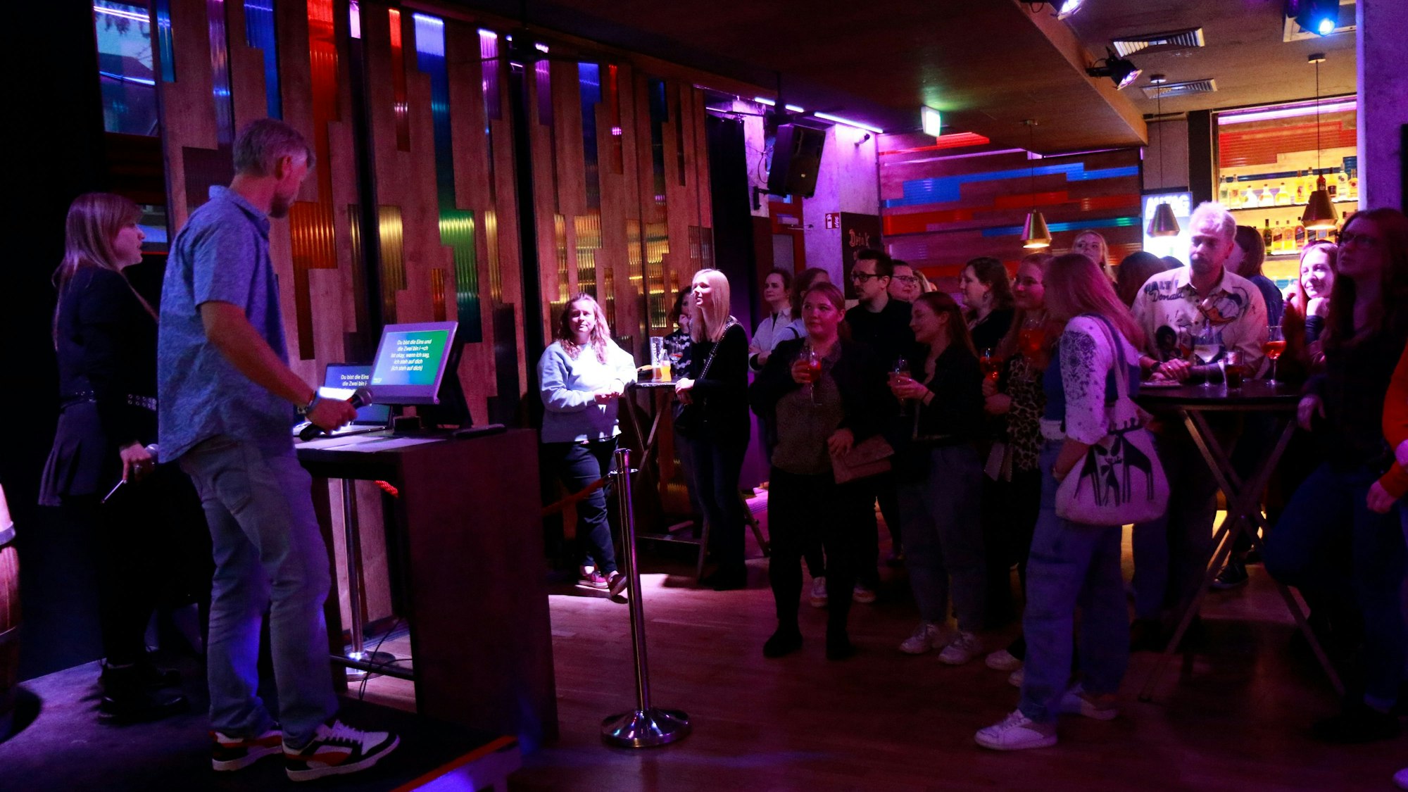 Eine Menschengruppe steht vor einem Pult in einem spärlich beleuchteten Raum und singt.