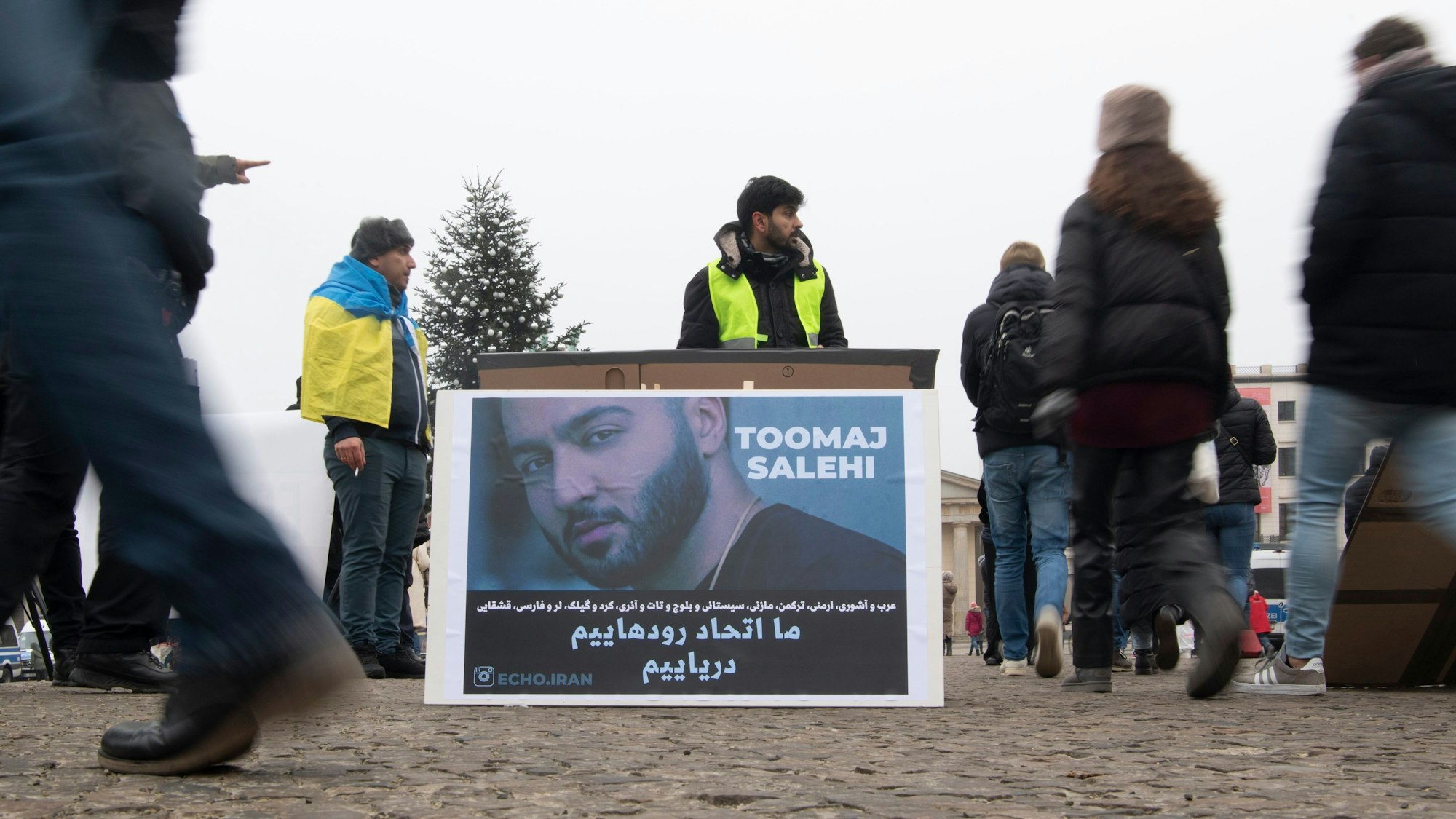 Ein großes Plakat steht bei einer Protestaktion gegen Irans Staatsführung auf dem Pariser Platz. Es zeigt den iranischen Rapper Toomaj Salehi.