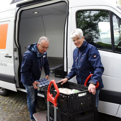 Das Foto zeigt eine Frau und einen Mann, die Lebensmittel aus einem Auto ausladen.