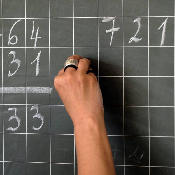 Eine Lehrerin schreibt Mathematikaufgaben auf eine Schultafel.