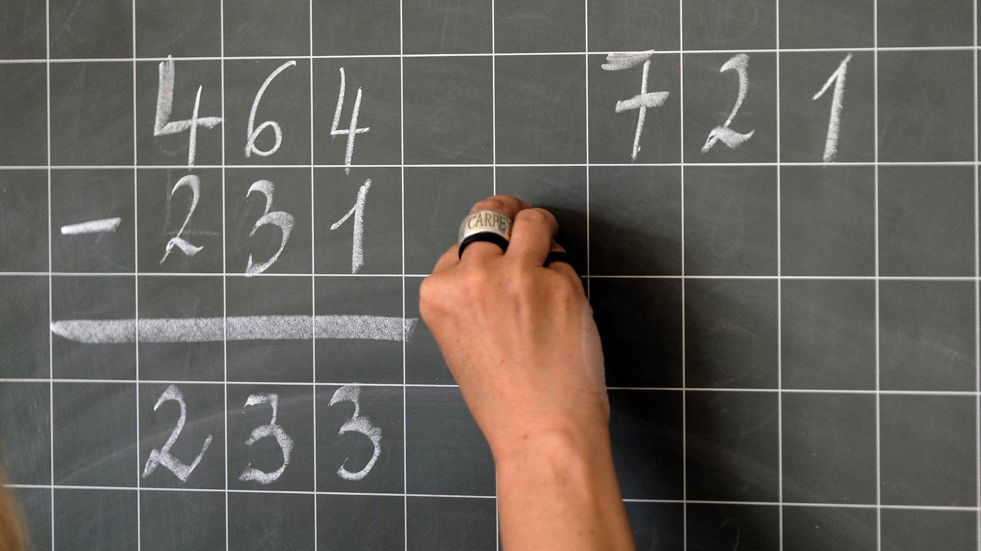 Eine Lehrerin schreibt Mathematikaufgaben auf eine Schultafel.