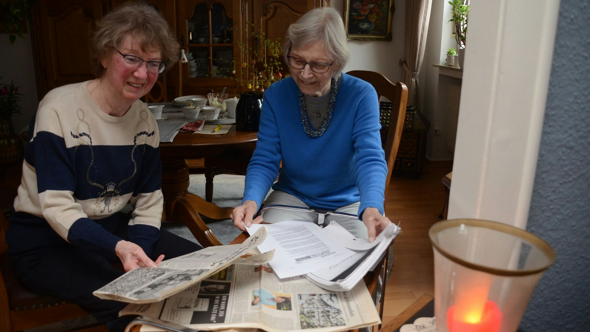Zwei Seniorinnen blicken auf alte Zeitungsberichte.