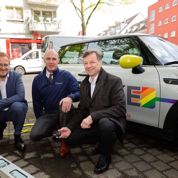 Drei Männer knien vor einem E-Auto, das an einer neuen Ladestation geladen wird.
