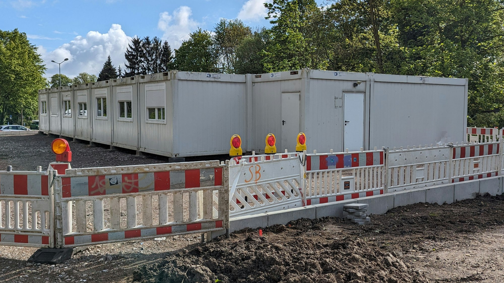 Wohncontainer stehen hinter einem Baustellenzaun an einer Straßenecke.