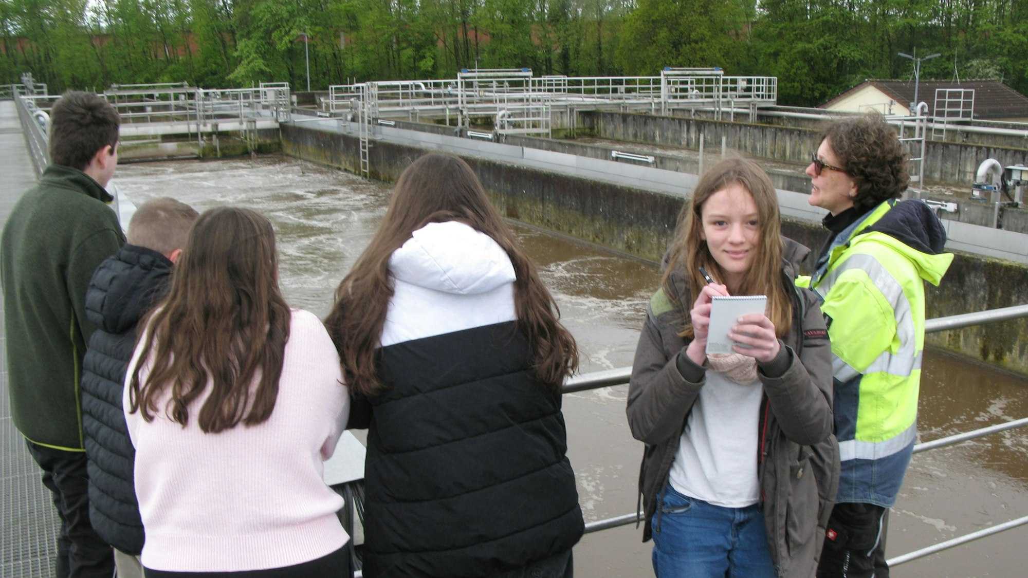 Redaktionskind Mona Friedrich (10) steht am Wiederbelebungsbecken der Hennefer Zentralkläranlage mit den Tagespraktikanten und Alexandra Thielen.