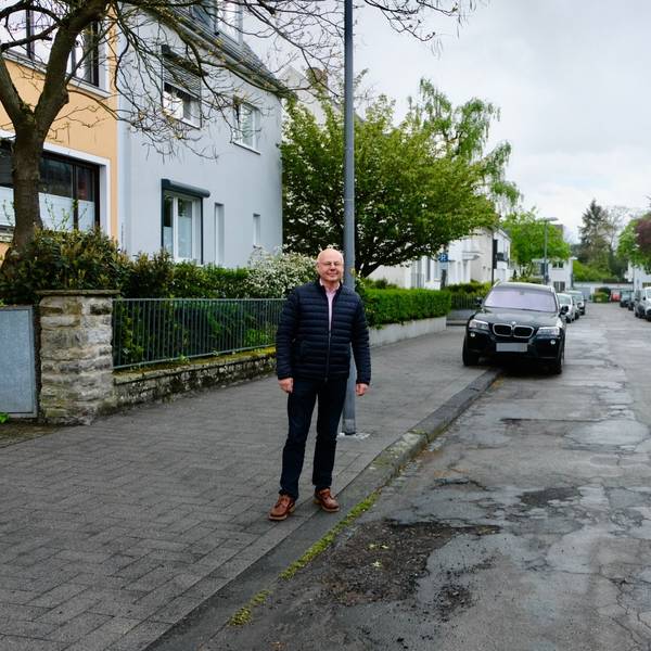 Joachim Hüttl auf dem frisch gepflasterten Gehweg der Von-Lauff-Straße neben der löchrigen Fahrbahn.