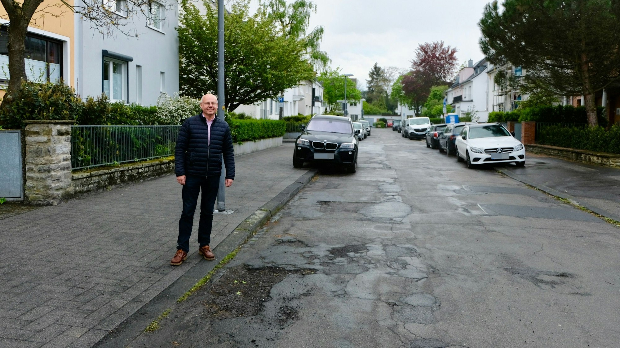 Joachim Hüttl auf dem frisch gepflasterten Gehweg der Von-Lauff-Straße neben der löchrigen Fahrbahn.