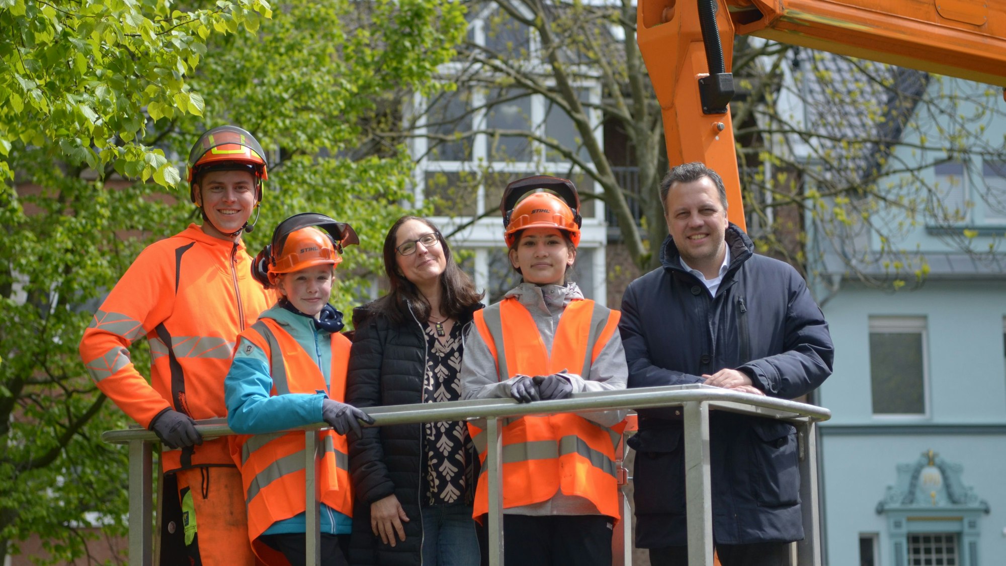 Die beiden Mädchen und die Vertreter der Stadt stehen auf der Arbeitsplattform eines Hubwagens, der für Baumpflegearbeiten eingesetzt wird.