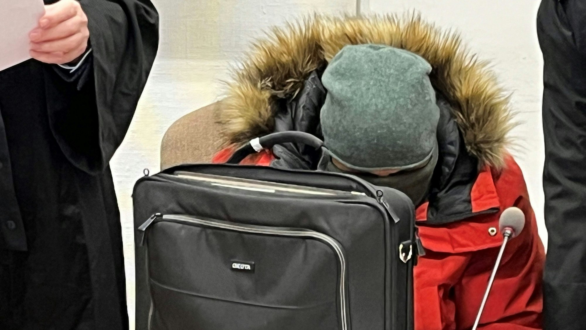 Prozessauftakt am 29. Januar 2024 vor dem Kölner Landgericht: Der mit einem Schal vermummte Angeklagte, der  wegen gewerbsmäßigen Betruges mit Coronatests einen Schaden von 19 Millionen Euro verusacht haben soll, versteckt sich hinter einem Aktenkoffer.