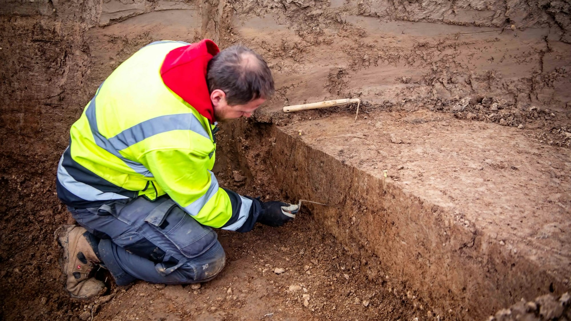 Das Bild zeigt den Grabungstechniker des LVR bei seiner Arbeit. Er kratzt mit einer kleinen Schaufel im Dreck.