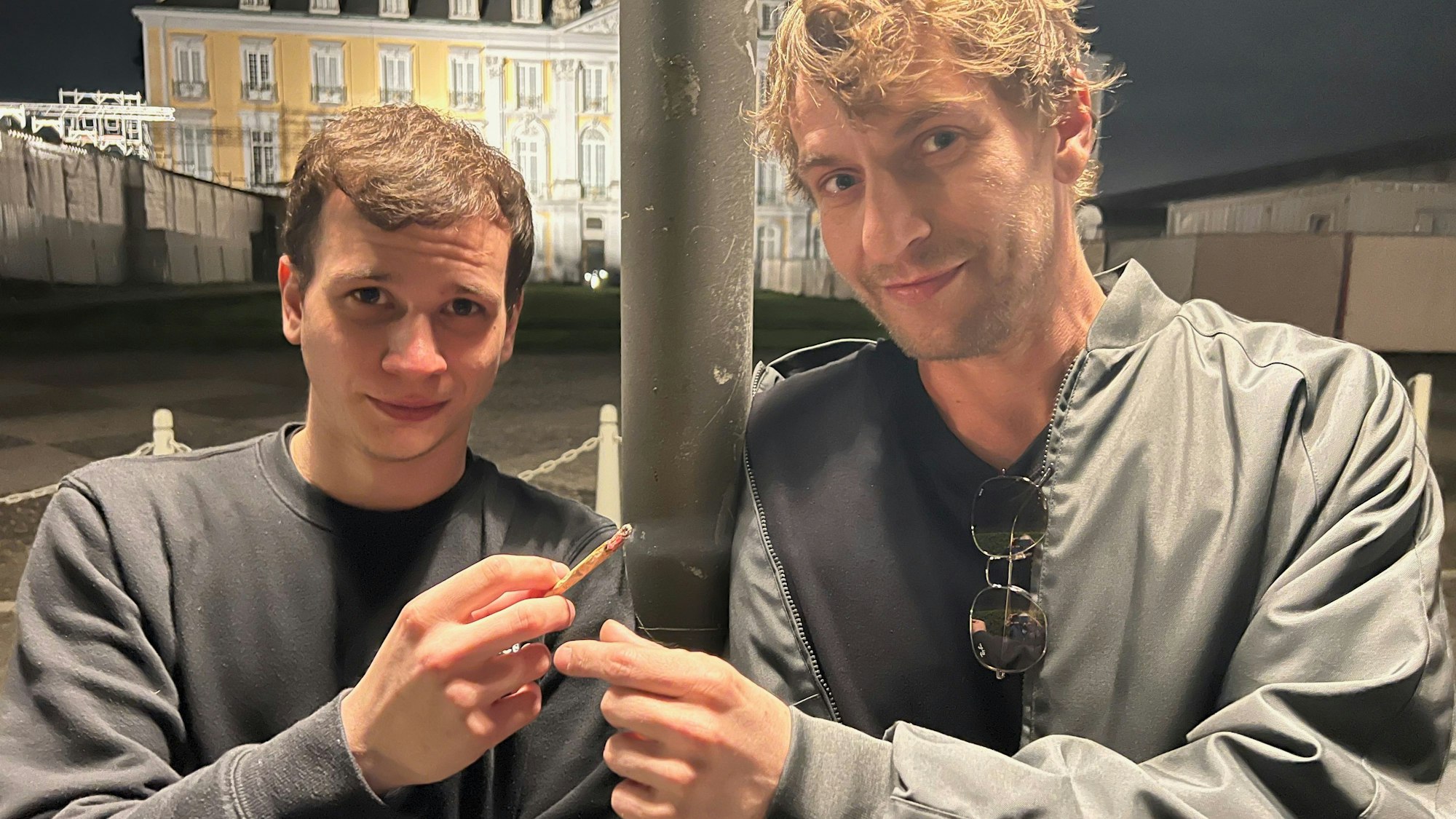 Auf dem Foto sind Janni und Sven Steiger vom Cannabis-Club Brühl zu sehen. Sie stehen vor Schloss Brühl und rauchen einen Joint.
