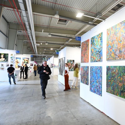 Das Treiben auf der Kunstmesse Discovery Art Fair 2024 am 25.04.2024 in Köln. Im Vordergrund sind bunte Pop-Art-Werke zu sehen. Foto von Alexander Schwaiger.