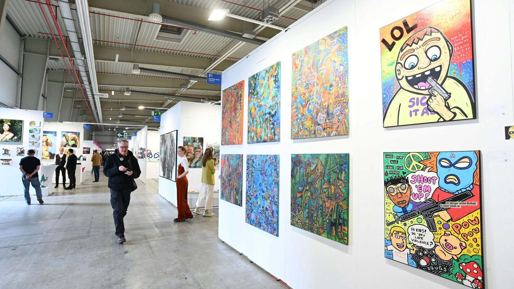 Das Treiben auf der Kunstmesse Discovery Art Fair 2024 am 25.04.2024 in Köln. Im Vordergrund sind bunte Pop-Art-Werke zu sehen. Foto von Alexander Schwaiger.