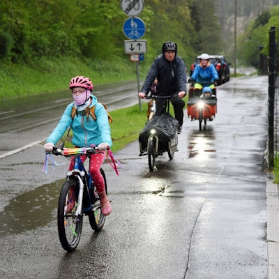 Kinder und Erwachsene auf Fahrrädern fahren entlang einer nassen Straße.