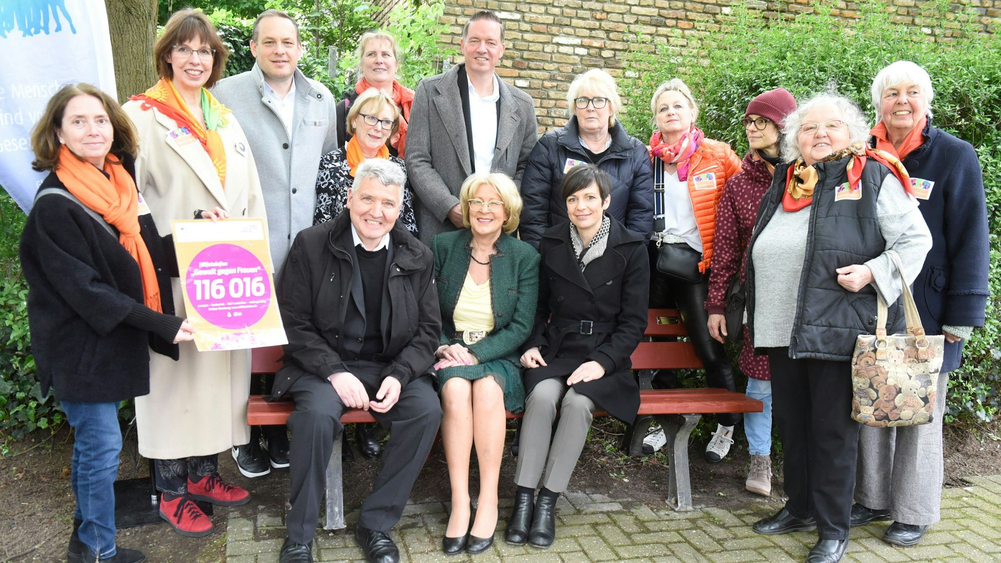 Zu sehen ist eine Gruppe von Menschen auf und rund um eine Bank.