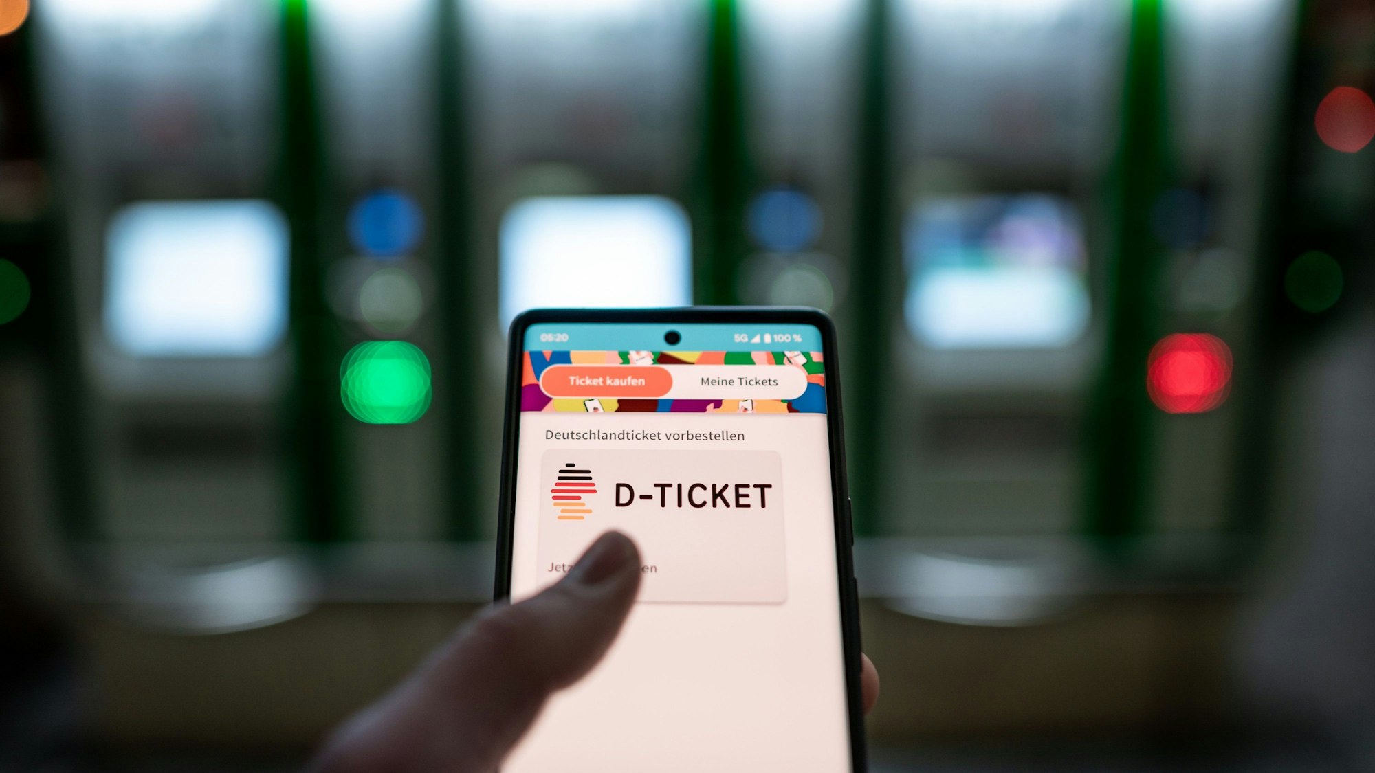 Ein Mann hält ein Mobiltelefon, auf dem das „D-Ticket“ gekauft werden kann, vor Ticketautomaten am Hauptbahnhof in der Hand.