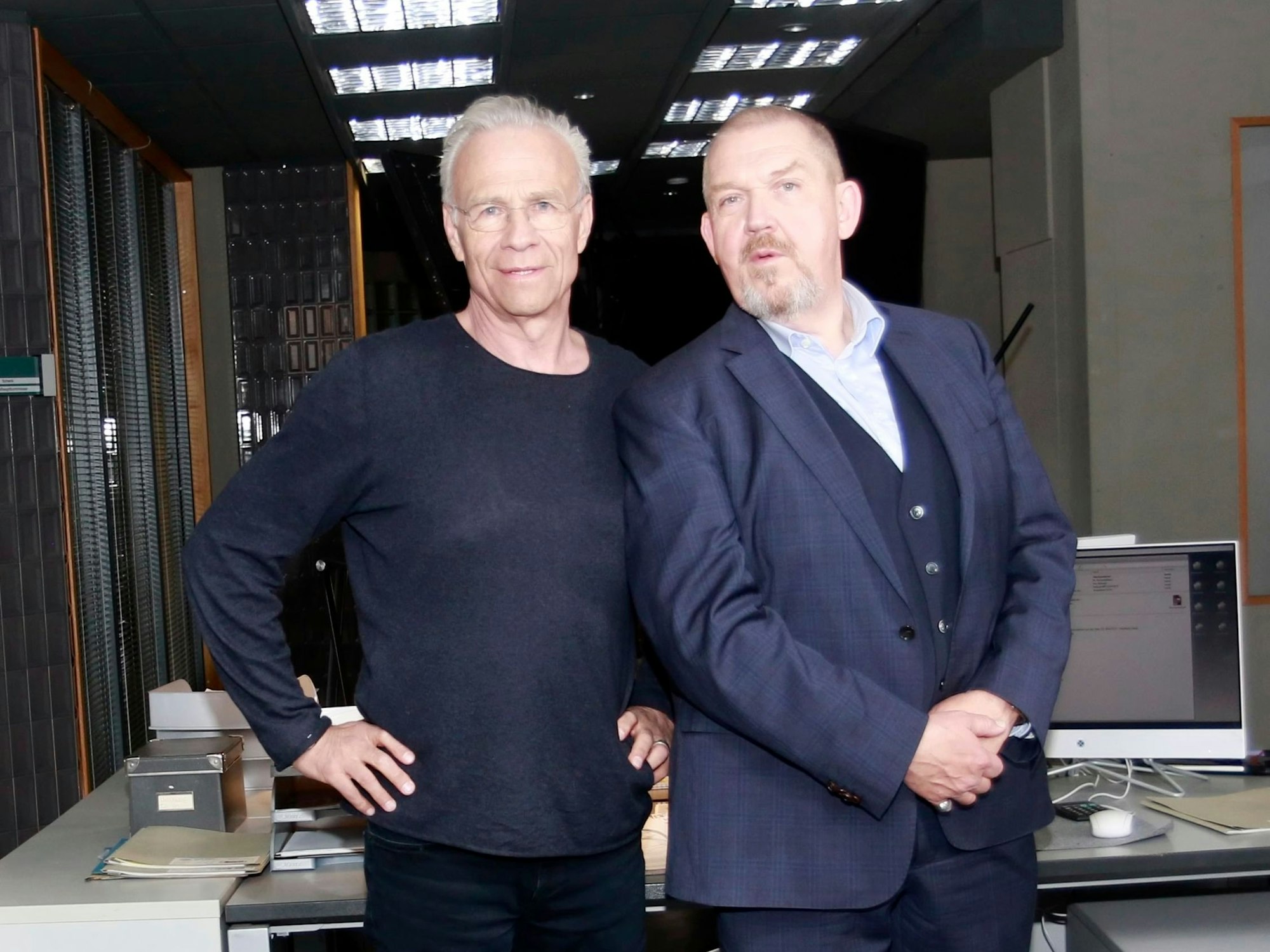 Zwwei Männer stehen vor einem Schreibtisch.