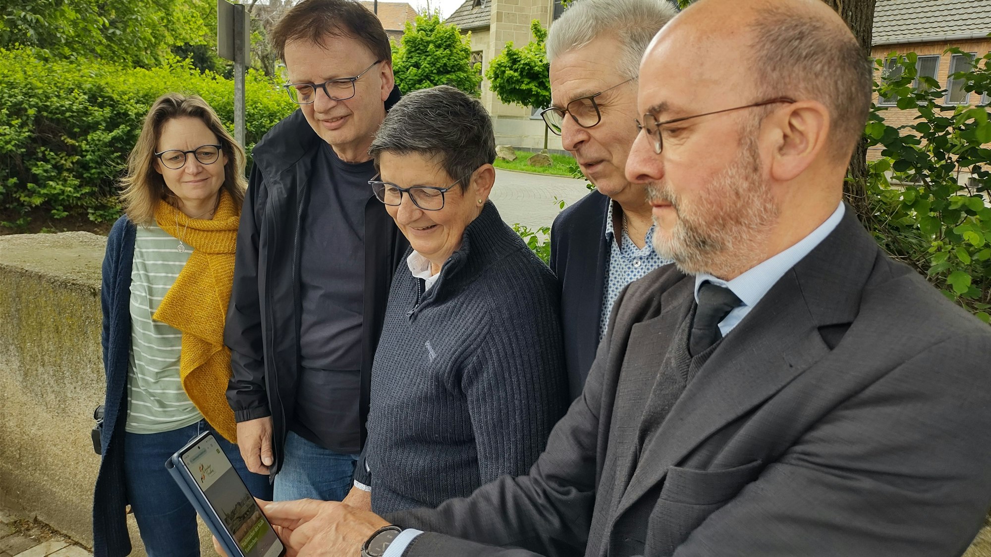 Werner Jacobs hat auf dem Handy die Homepage des Projekts „Lebendiger Friedhof“ aufgerufen, die anderen Projekt-Mitwirkenden schauen mit ihm darauf.