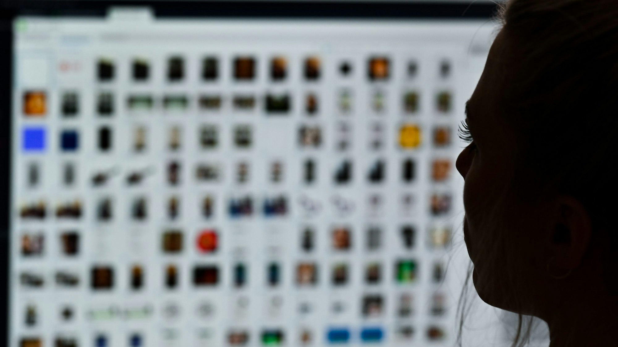 Auf einem unscharfen Bildschirm sind Kästchen zu sehen, auf die eine Frau im Dunkeln schaut. (Symbolbild)