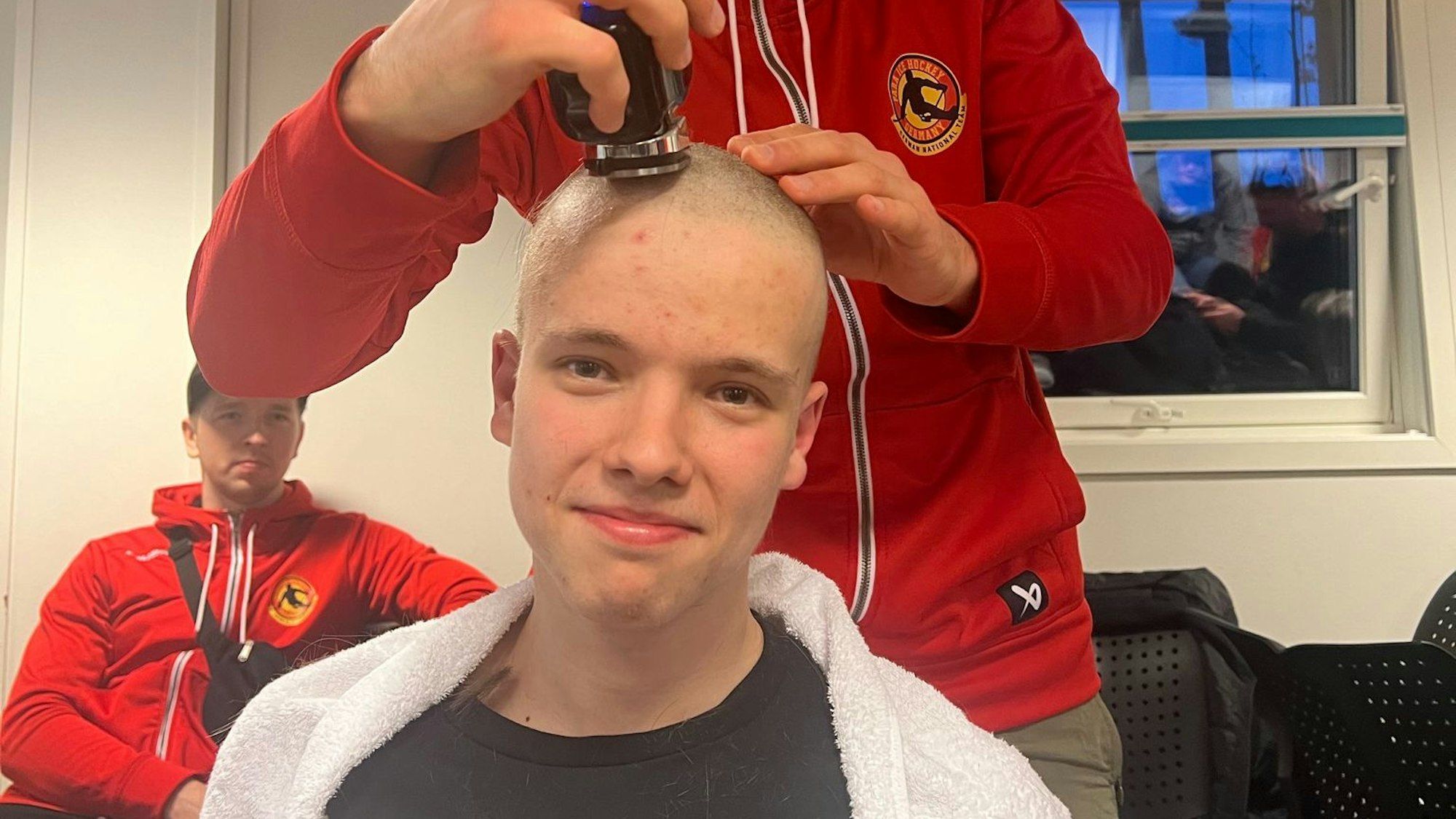 Ein junger Mann rasiert einem anderen jungen Mann die Kopfhaare ab.