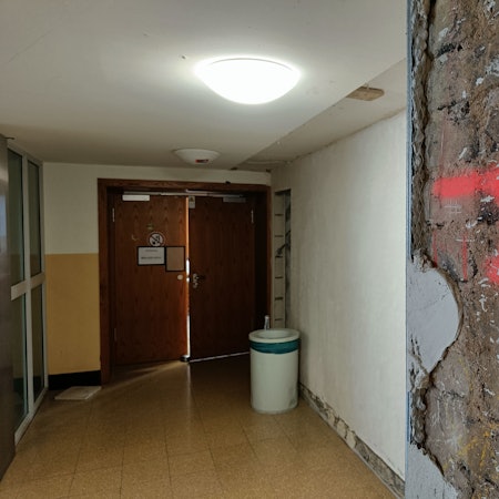 An einer Säule vor einem Hörsaal ist großflächig der Putz abgebröckelt.