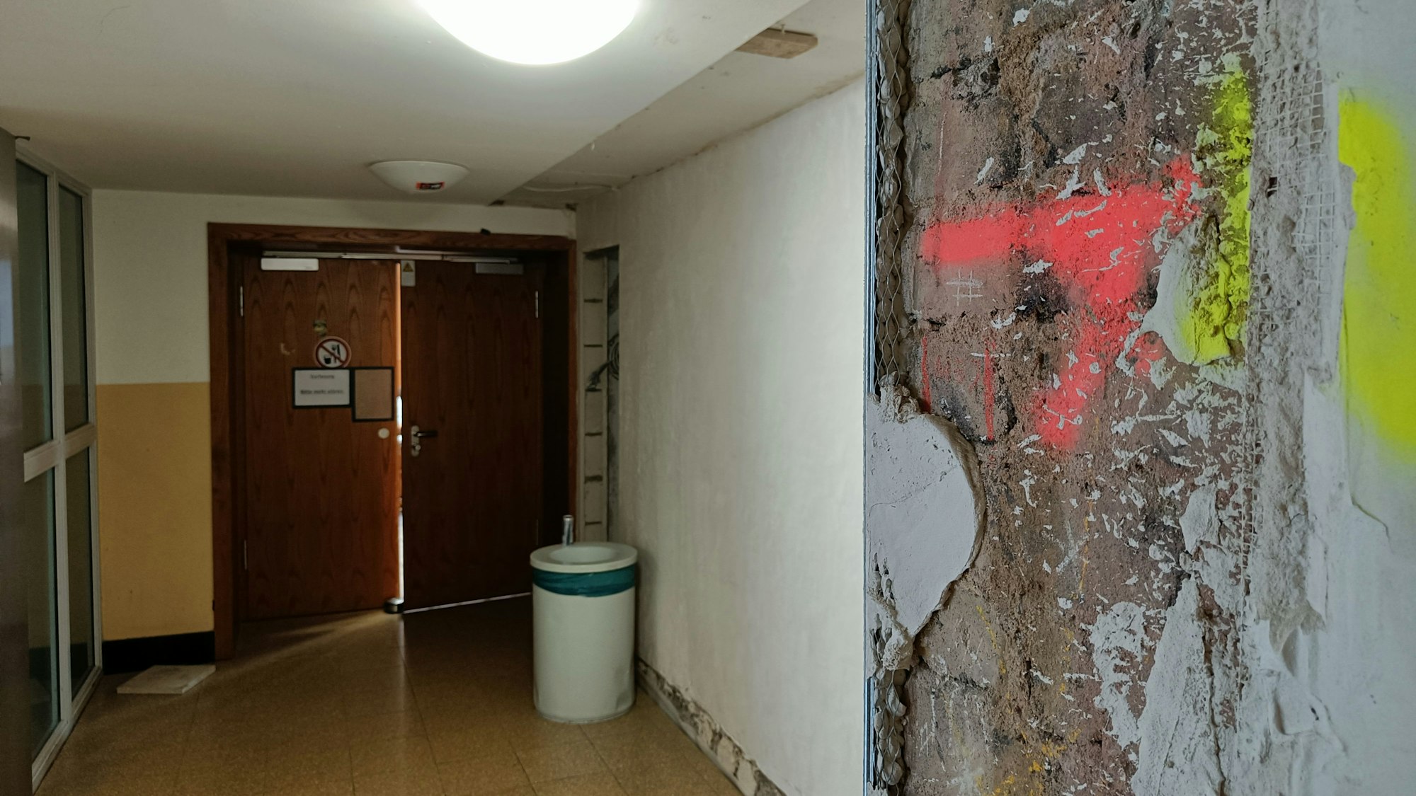 An einer Säule vor einem Hörsaal ist großflächig der Putz abgebröckelt.