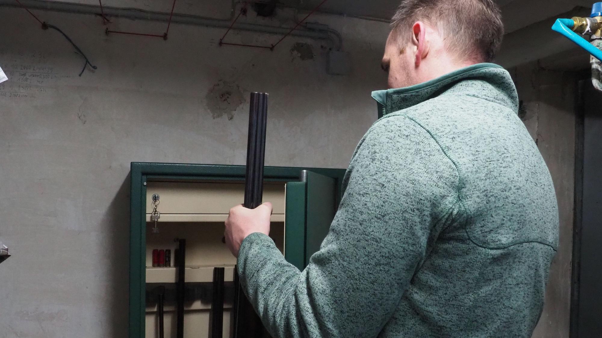 Ein Mann nimmt ein Gewehr aus einem Waffenschrank.