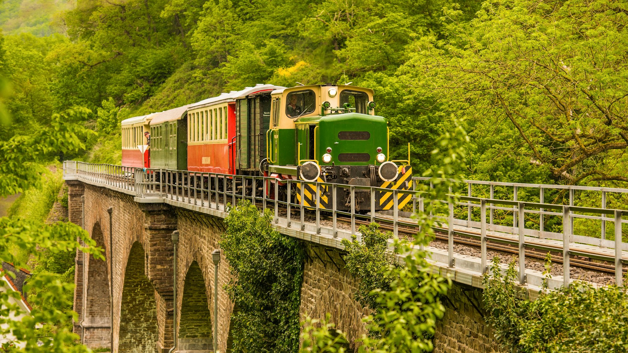 Grüne Dampflokomotive fährt über einen alten Viadukt.