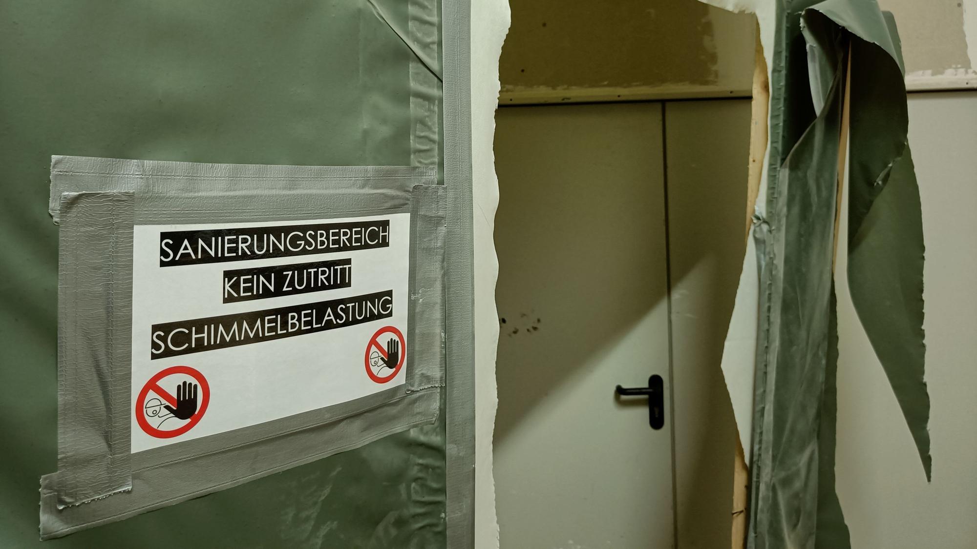 An einer grünen Plane klebt in Warnschild: „Sanierungsbereich, kein Zutritt, Schimmelbelastung“