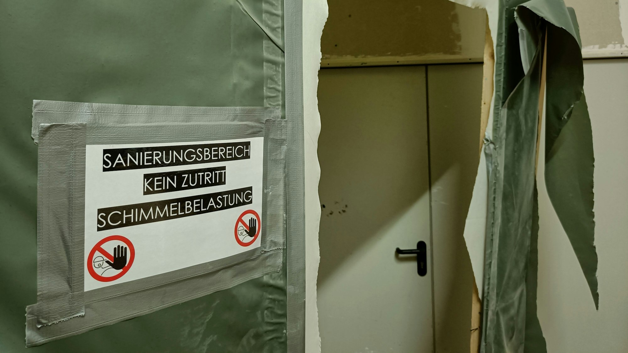 An einer grünen Plane klebt in Warnschild: „Sanierungsbereich, kein Zutritt, Schimmelbelastung“