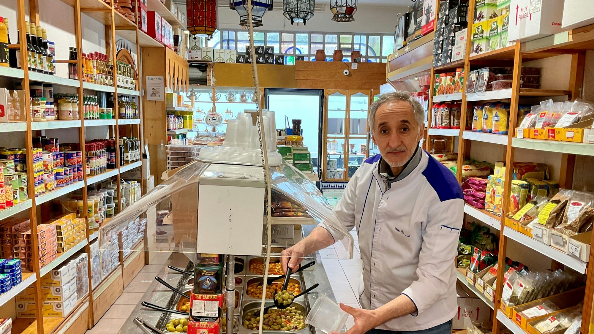 Mann schöpft im Geschäft aus einer Oliven-Auswahl