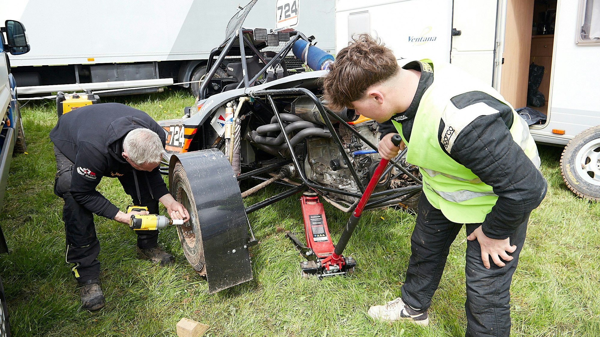 Ein Mann schraubt ein Rad eines Autocross-Fahrzeugs fest, sein Sohn im Teenager-Alter hält den Wagenheber.