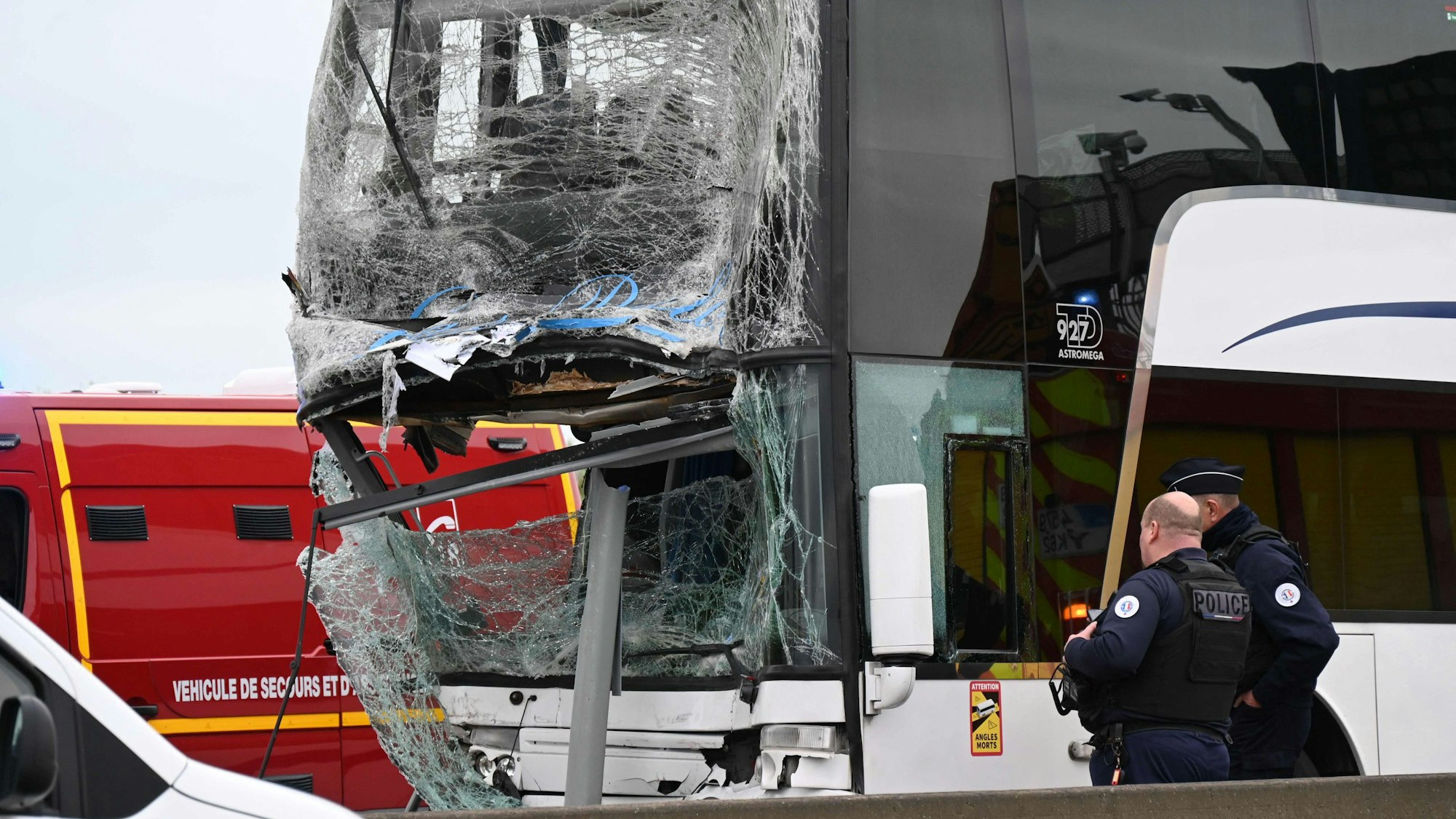 Das Bild zeigt einen Bus, der nach einer Kollision stark beschädigt ist. Zwei Polizisten schauen sich den Bus an.