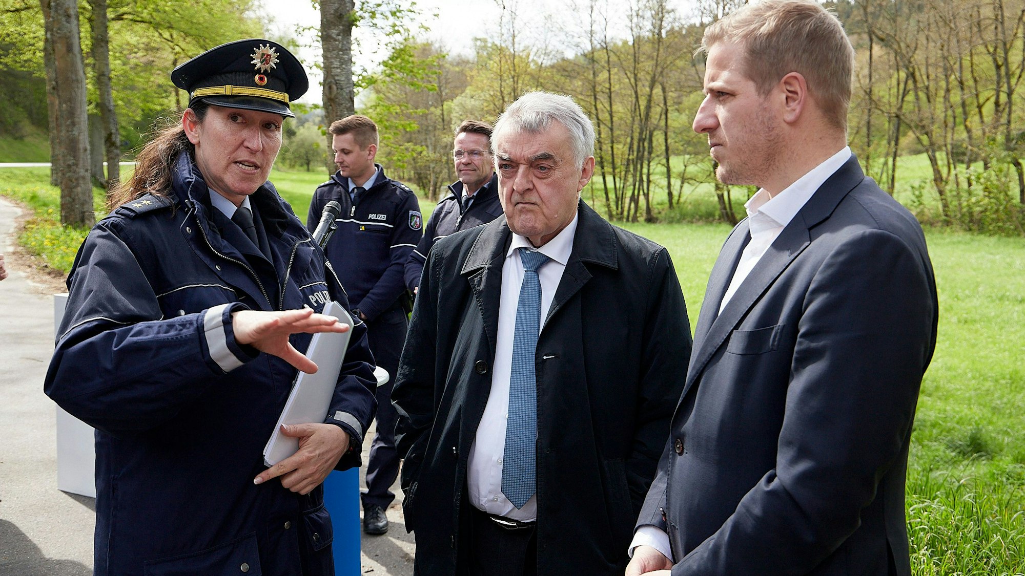 Martina Mensching, Landesinnenminister Herbert Reul und Landrat Markus Ramers (v.l.) stehen gemeinsam auf einem Parkplatz an der B258. Im Hintergrund sind weitere Polizisten zu sehen.