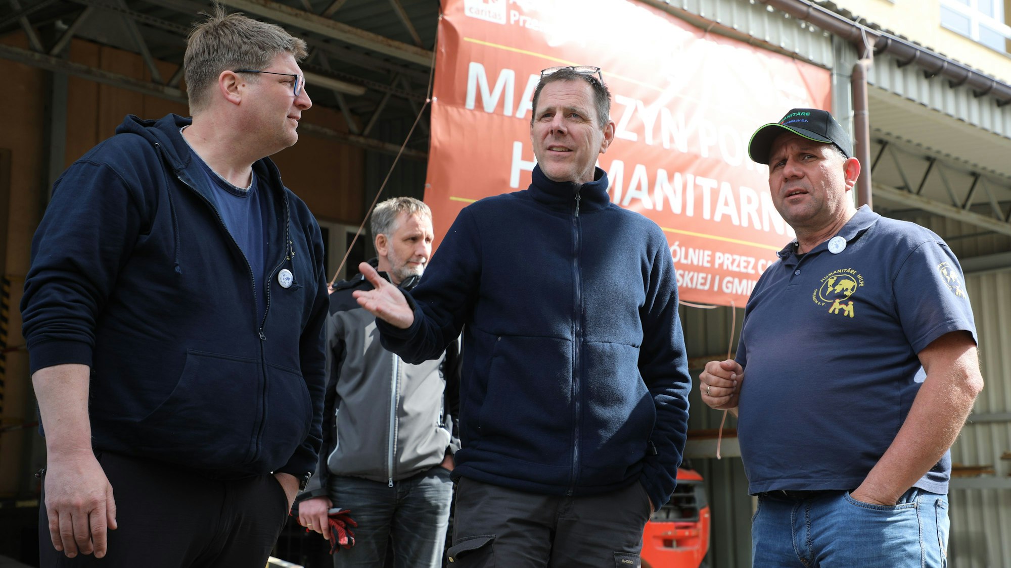Drei Männer stehen vor einem Banner des vormaligen Caritas-Transitlager an der polnisch-ukrainischen Grenze.
