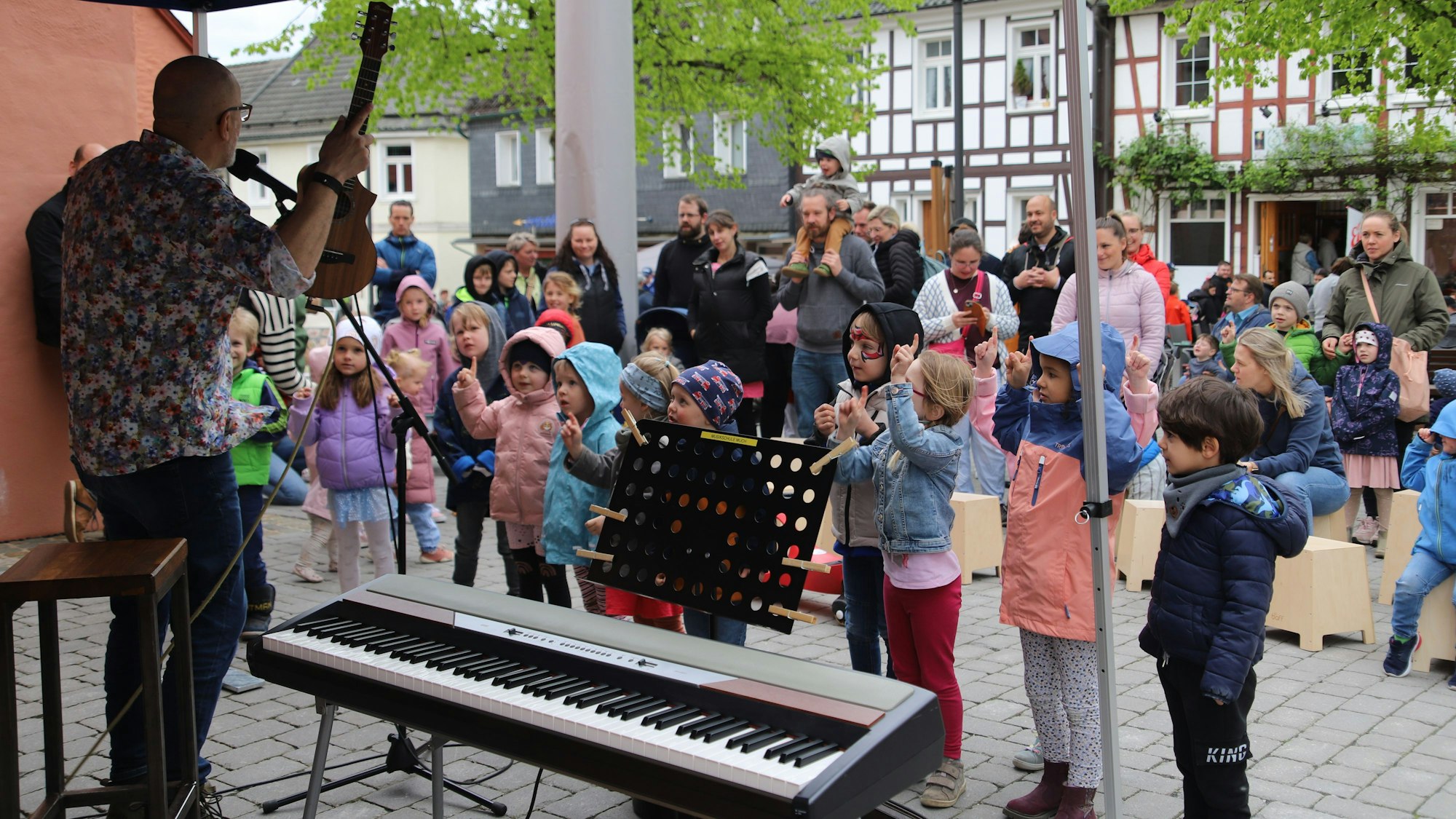 Paul Radau gab vor der Kirche ein Kinder-Mitmachkonzert. Kinder stehen vor dem Musiker und bewegen sich zu seinen Ansagen.