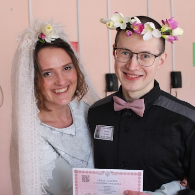 Evgenia Kulakova undViktor Filinkov, sie mit weißem Schleier, er mit Blumenkranz im Haar, bei der Hochzeit im Gefängnis. Beide lachen.