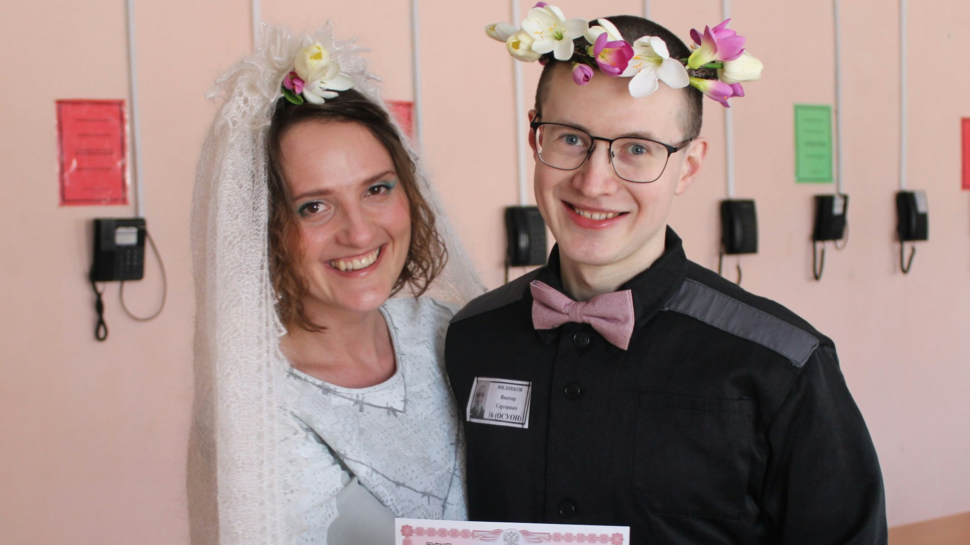 Evgenia Kulakova undViktor Filinkov, sie mit weißem Schleier, er mit Blumenkranz im Haar, bei der Hochzeit im Gefängnis. Beide lachen.