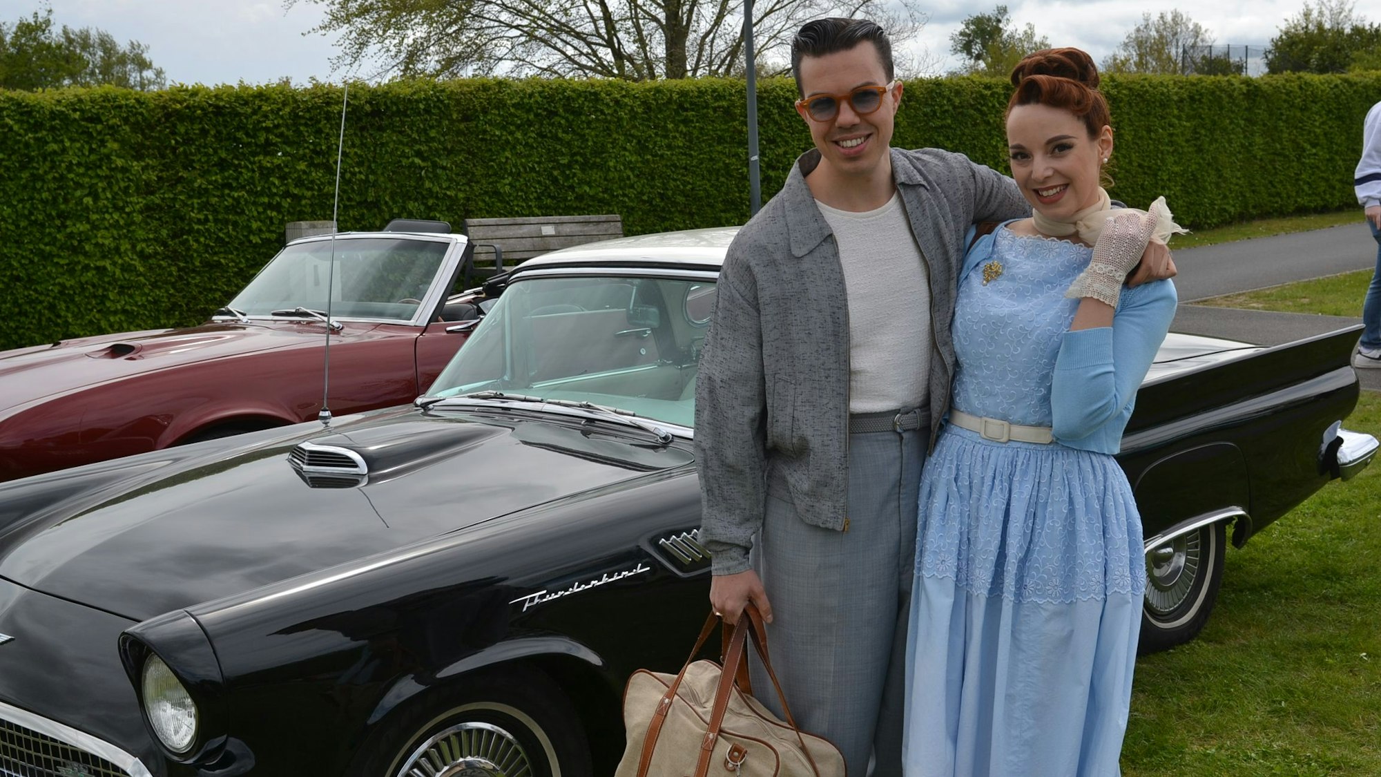 Das im Look der 50er Jahre gekleidete Paar posiert vor einem Straßenkreuzer.