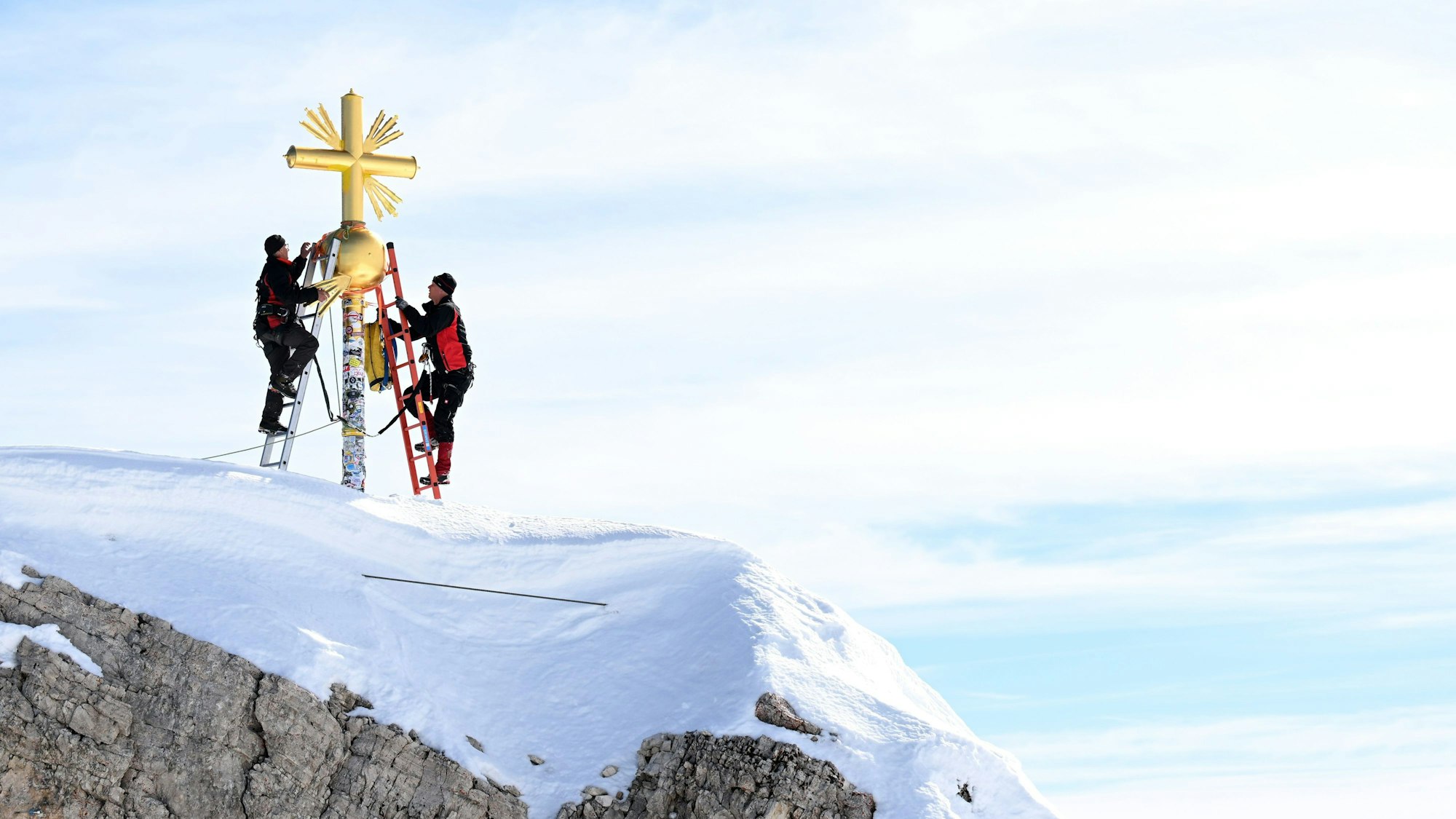 Zwei Personen bringen die im Tal restaurierten Strahlen des Gipfelkreuzes der Zugspitze wieder an.